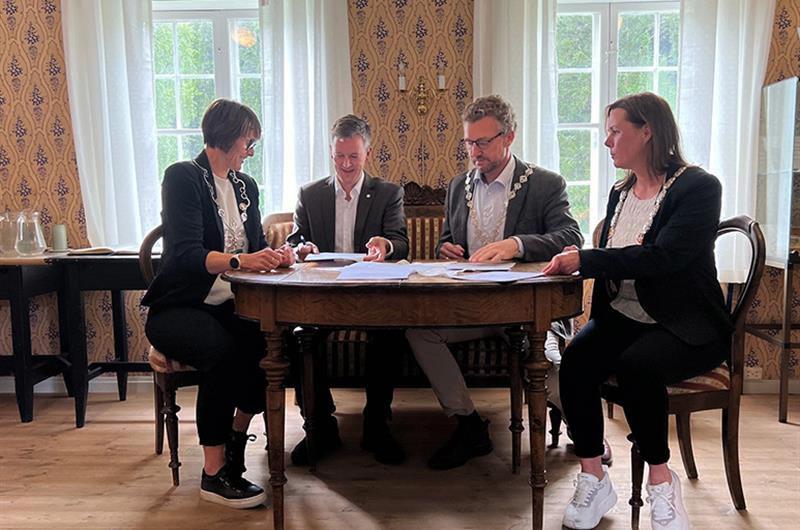 Fire personer sitter rundt et bord og signerer avtaler.