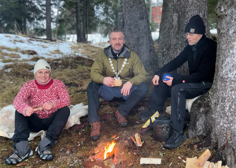 Tre personer sitter ved et bål.