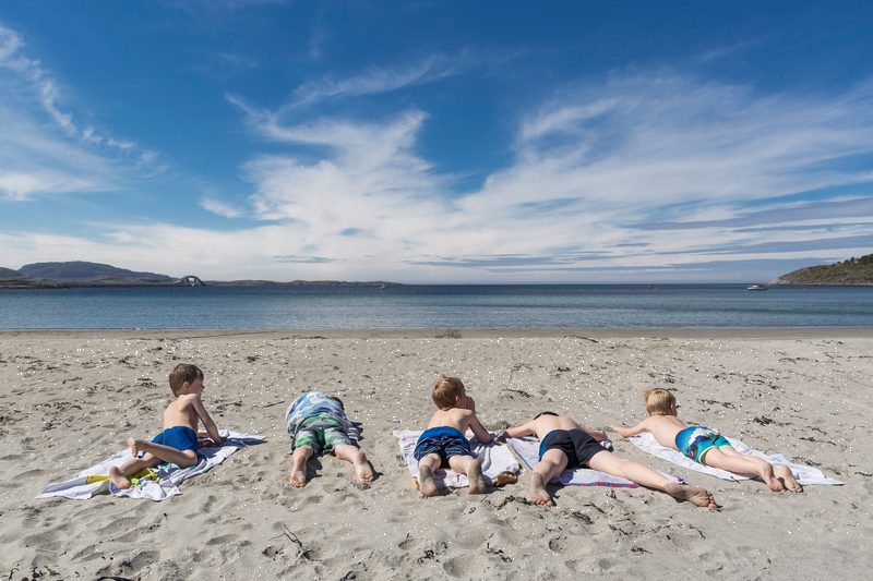 Fem gutter ligger på en sandstrand. 