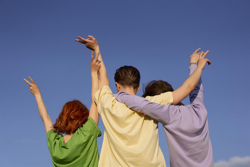 Bilde av tre ungdommer i naturen som tar high five med hverandre.