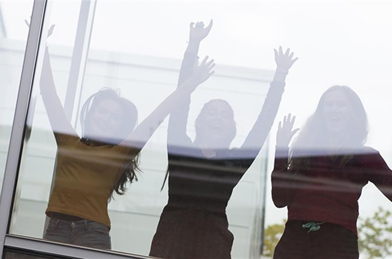 3 elever bak en glassvegg som strekker hendene i været